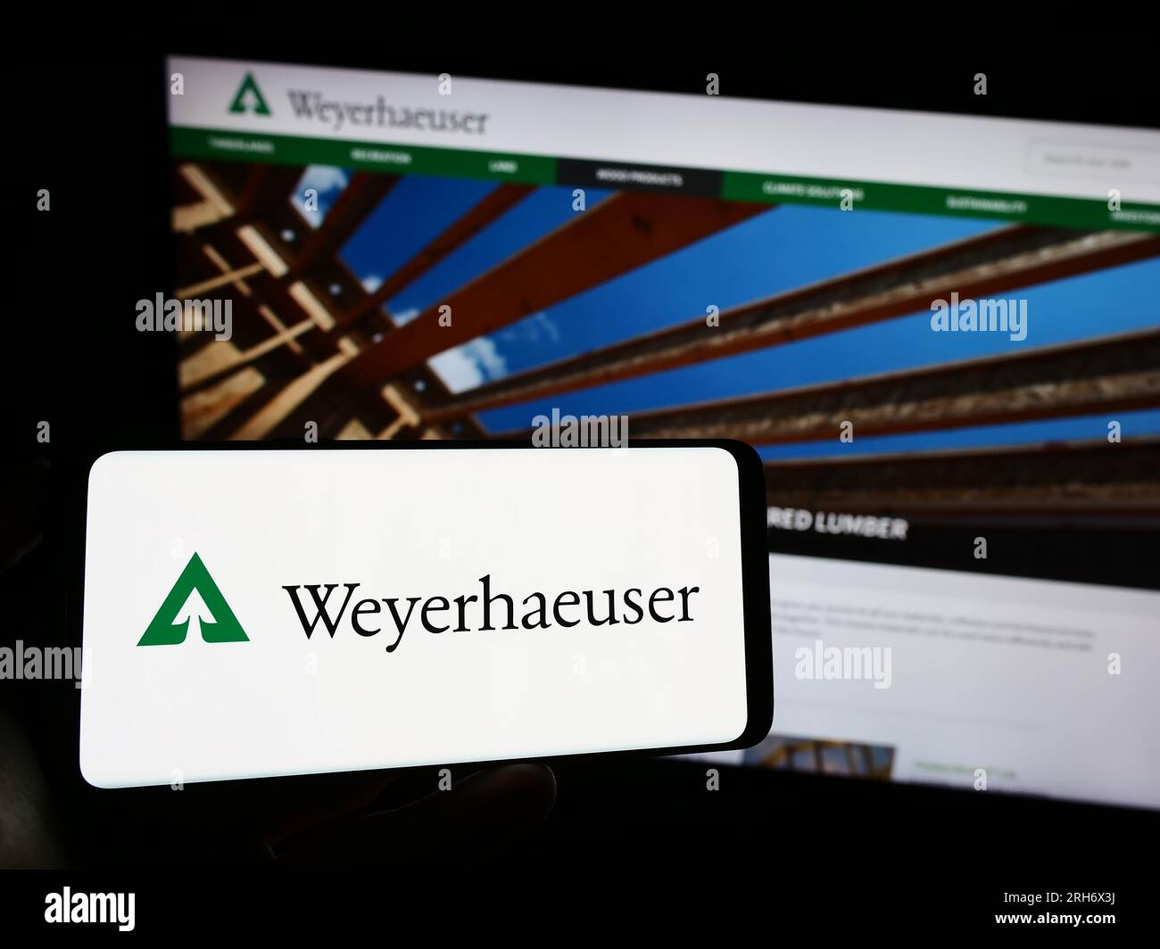 Person holding cellphone with logo of US timberland business Weyerhaeuser Company on screen in front of business webpage. Focus on phone display. Stock Photo