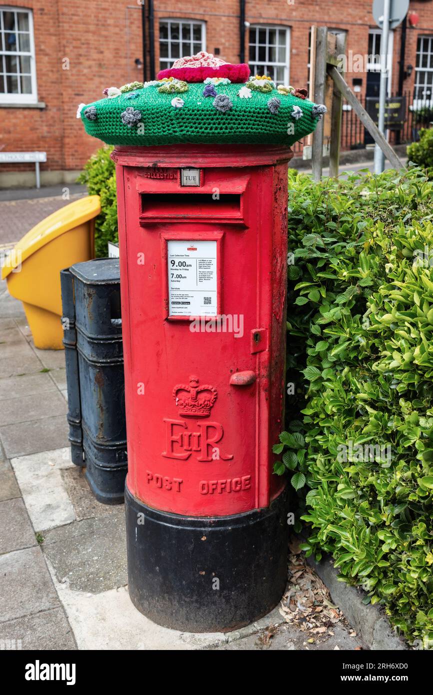 classic red post box decorated with a colourful knitted green hat in Hythe town centre kent Stock Photo