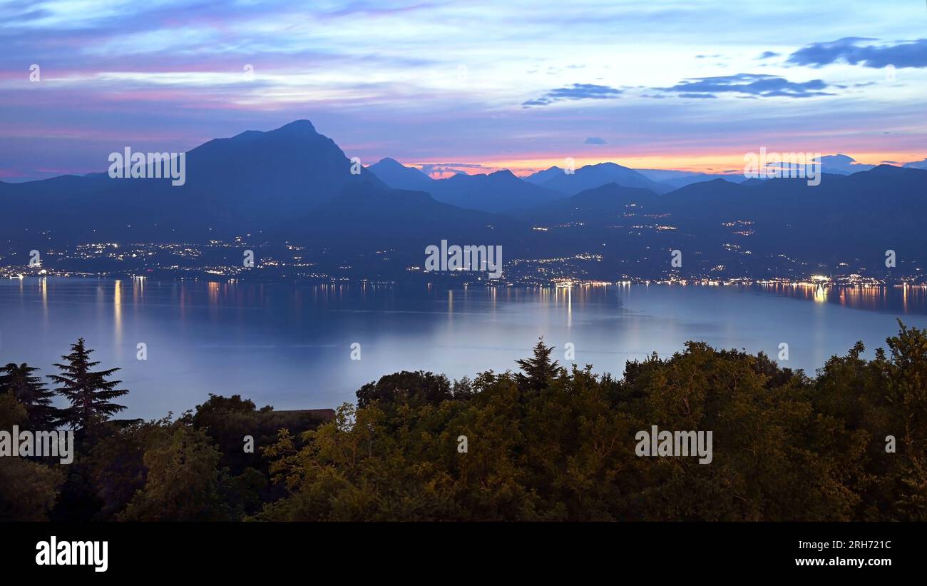 Mountains and trees with lights from Toscolano Maderno around lake Garda taken from San Zeno di Montagna at dusk in summer Stock Photo