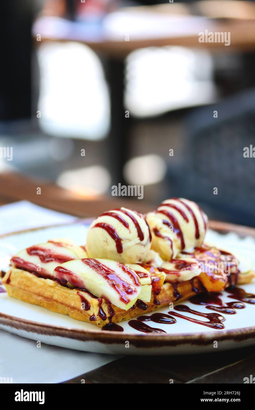 Belgian waffle with ice cream, berry sauce and fresh sliced fruits on a ...