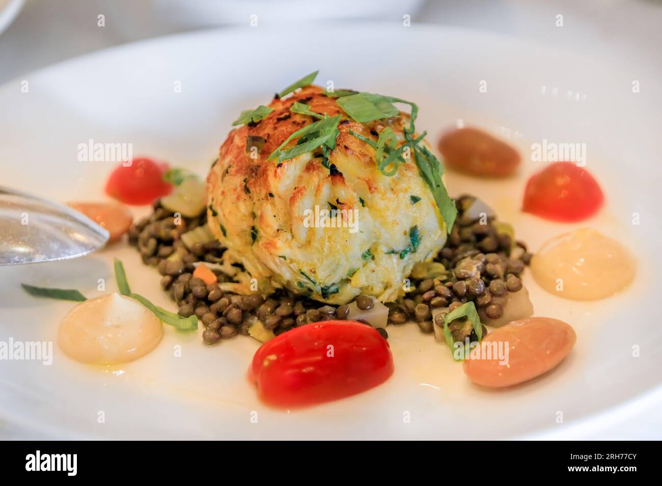 Large crab cake with lentils and cherry tomatoes on a plate at a high