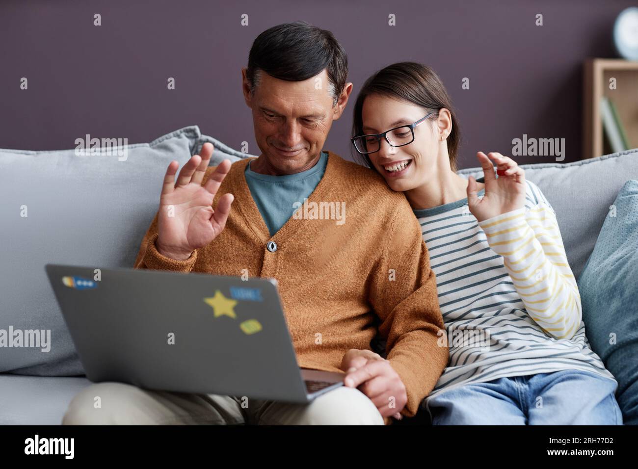 Portrait of father and teen daughter waving hello to video chat while  sitting on sofa with laptop Stock Photo - Alamy