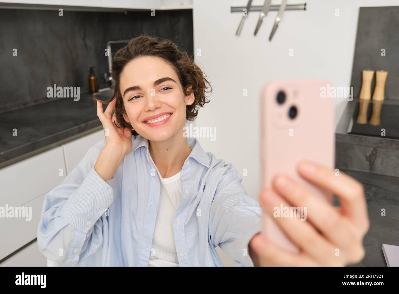 Happy, beautiful brunette girl takes selfie at home, poses for photo with smartphone. Stock Photo