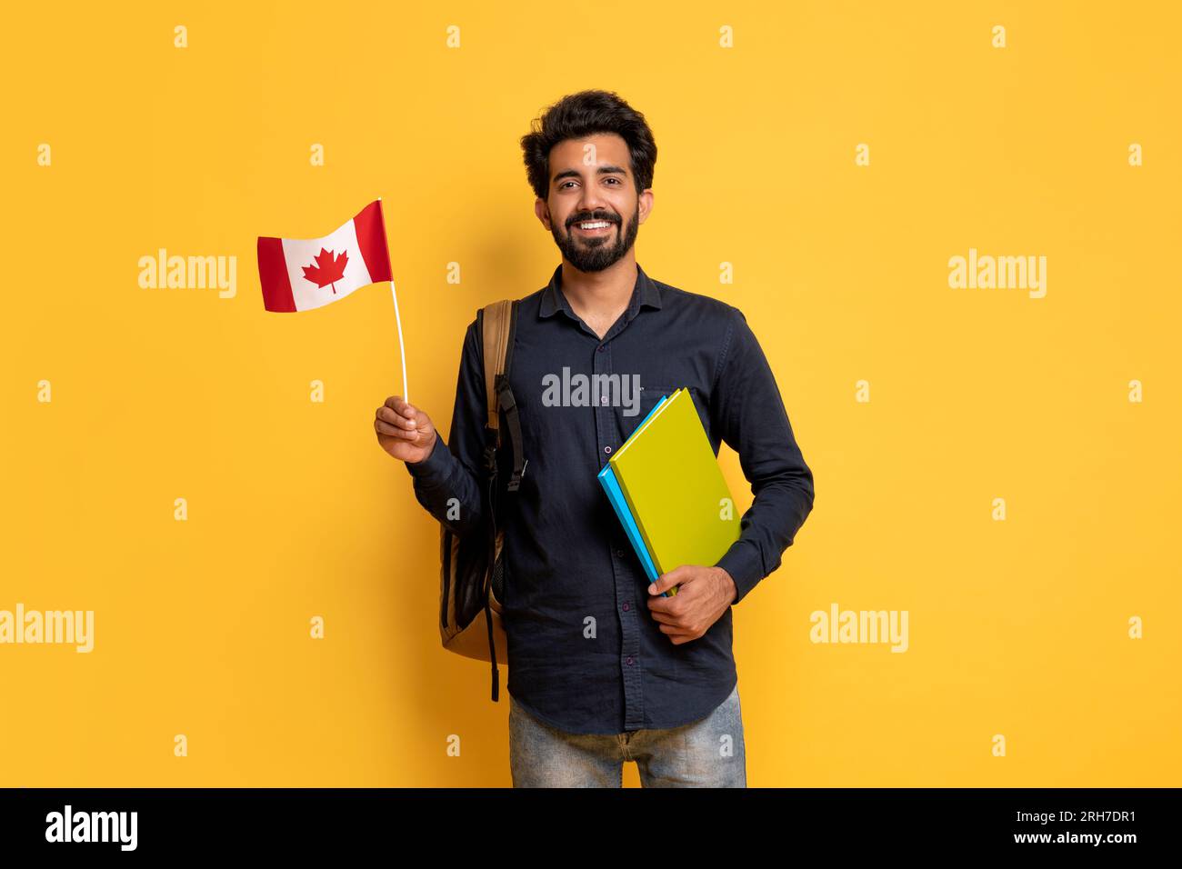 Smiling Indian Man With Canadian Flag And Workbooks Posing On Yellow Background Stock Photo
