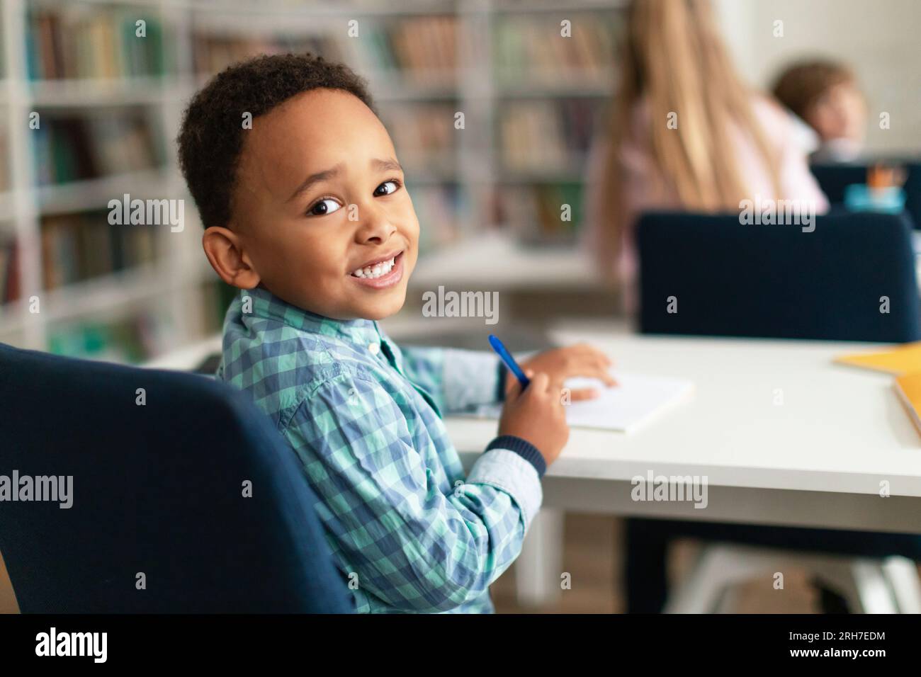 Portrait of african american schoolboy sitting at desk in classroom, turning back and smiling at camera, free space Stock Photo