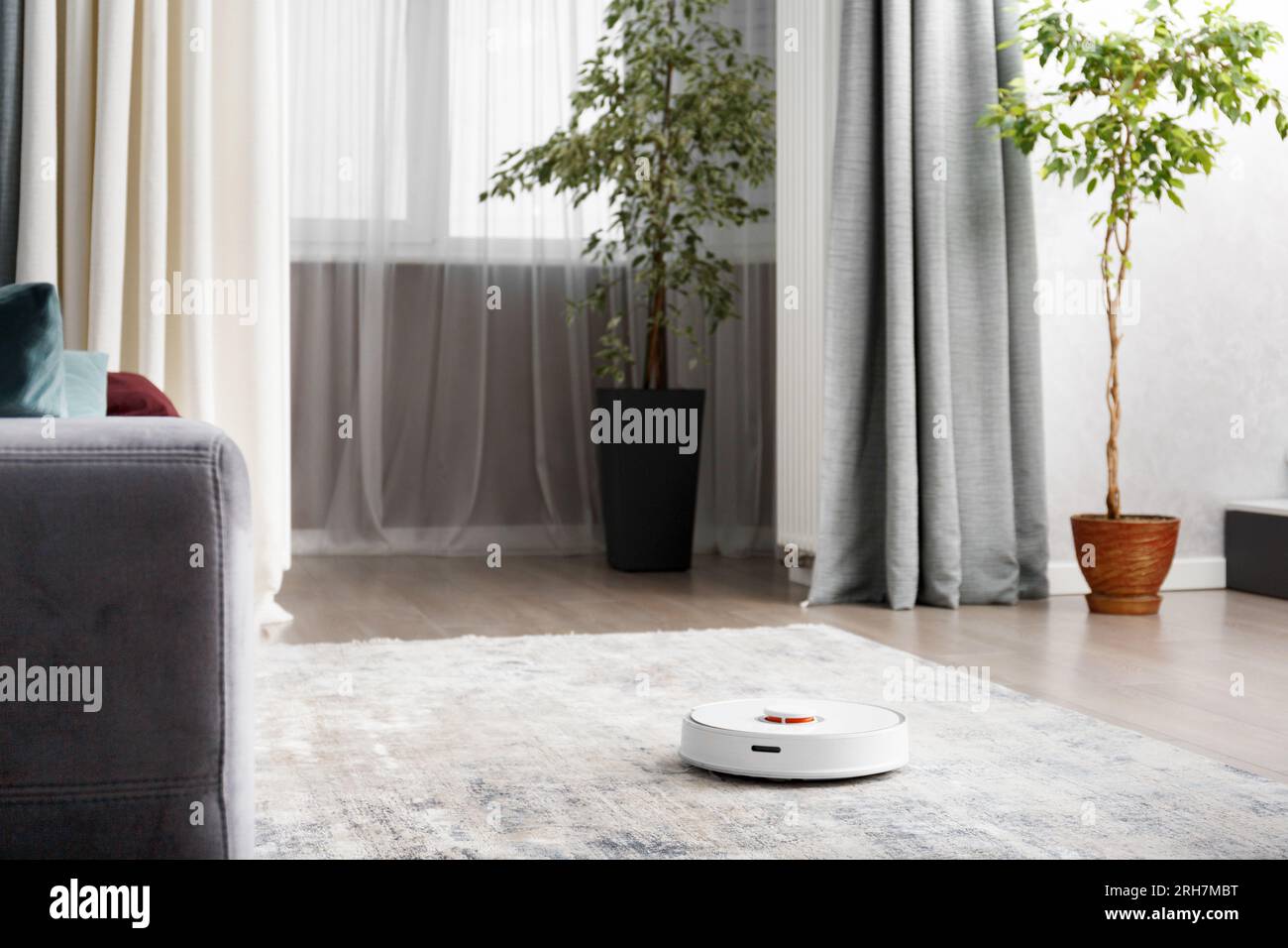 Smart robot vacuum cleaner in a modern living room interior. The concept of a smart home, wireless cleaning by a robot with a vacuum cleaner of any su Stock Photo