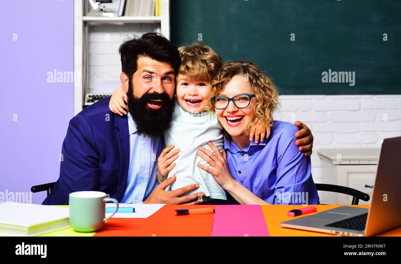 Back to school. Cute child boy from elementary school with teachers in classroom. Happy male and female teachers hugging with little schoolboy. Happy Stock Photo