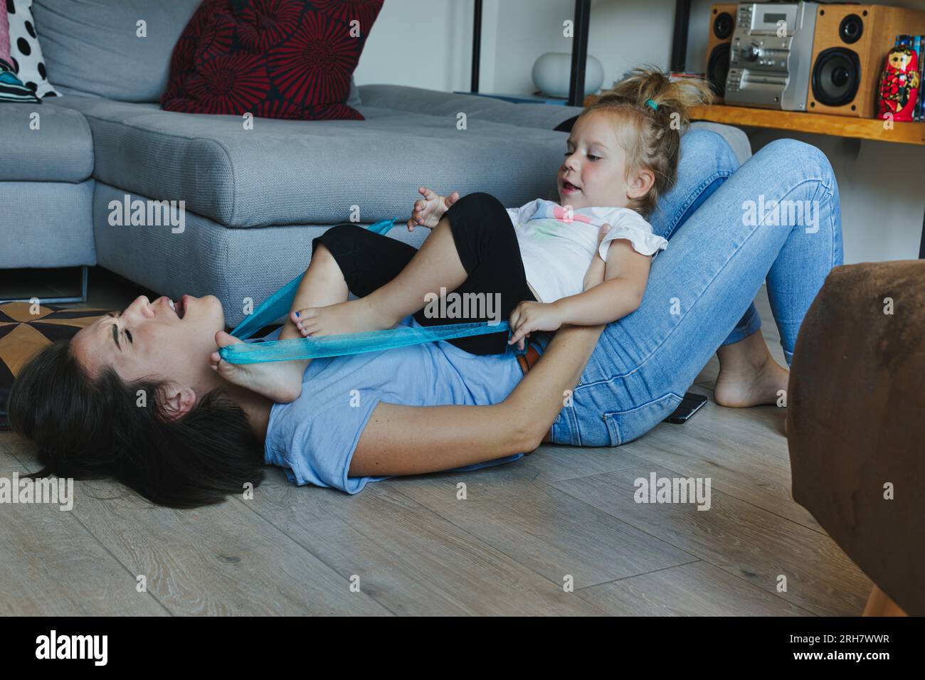 Joyful playtime: mother and daughter tangle in the living room, learning physical boundaries while also growing emotionally in a caring space Stock Photo