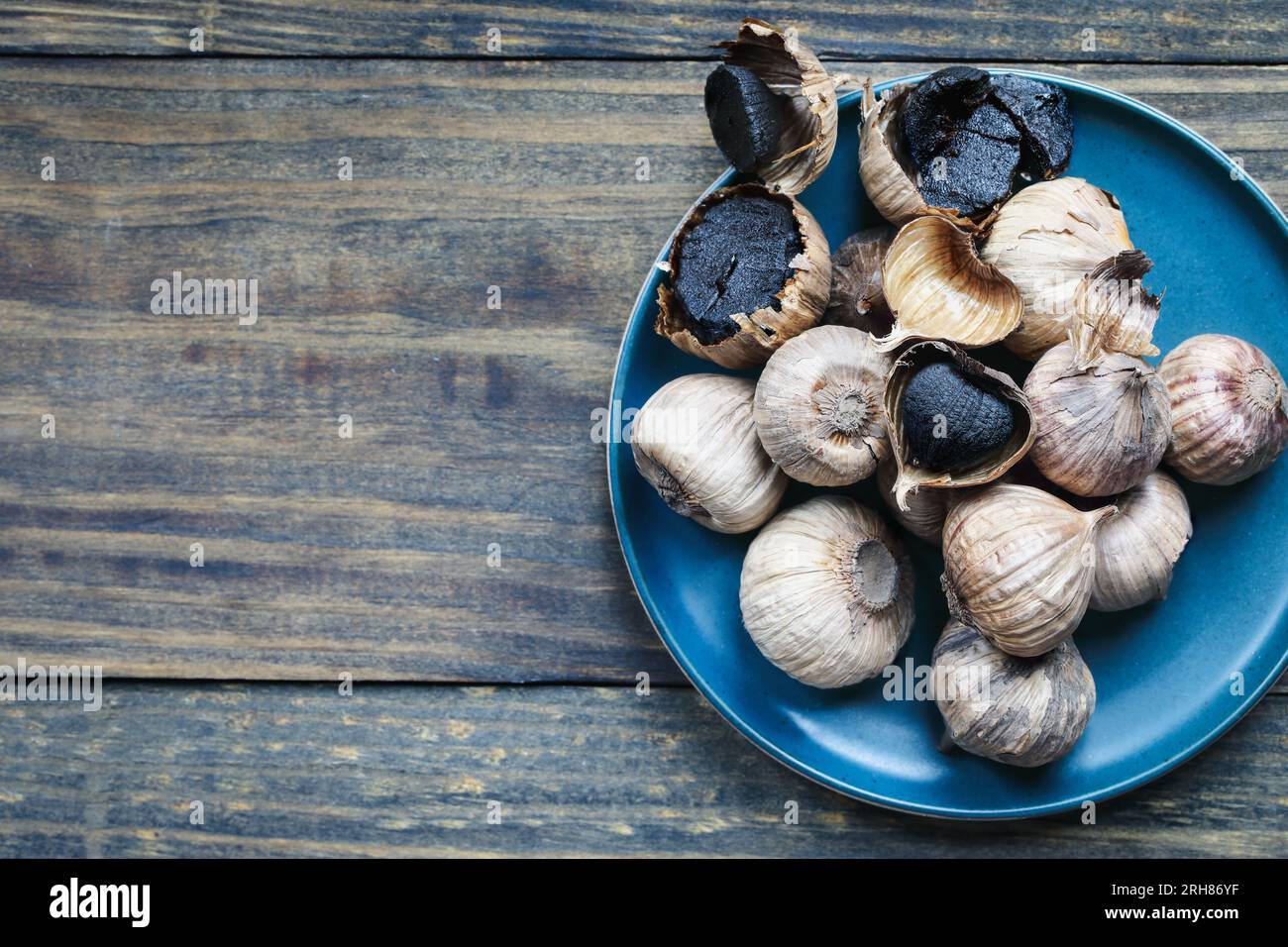 Table top view of black garlic cloves on a rustic wooden table with bulbs. Selective focus with blurred background and copy space. Stock Photo
