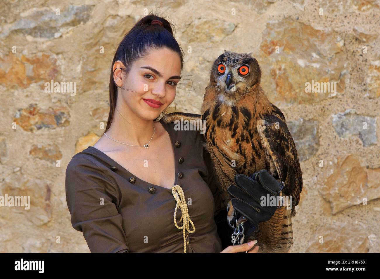 A female falconer holding a young Eurasian eagle-owl with big beautiful orange eyes at Golubac Fortress in Golubac, Serbia Stock Photo