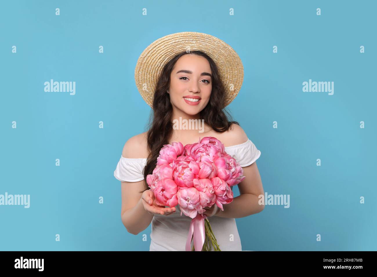 Beautiful young woman in straw hat with bouquet of pink peonies against ...