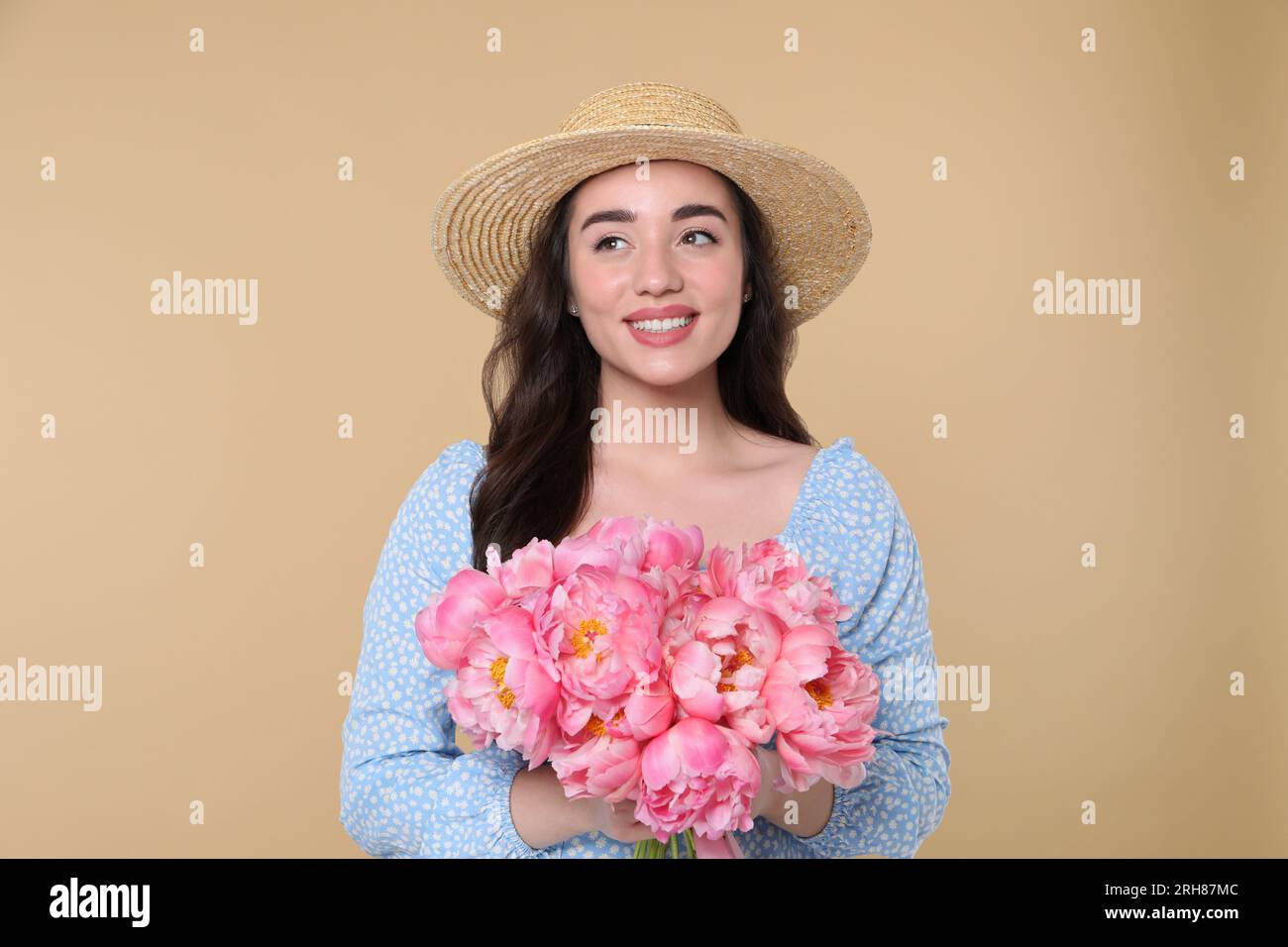 Beautiful young woman in straw hat with bouquet of pink peonies against ...