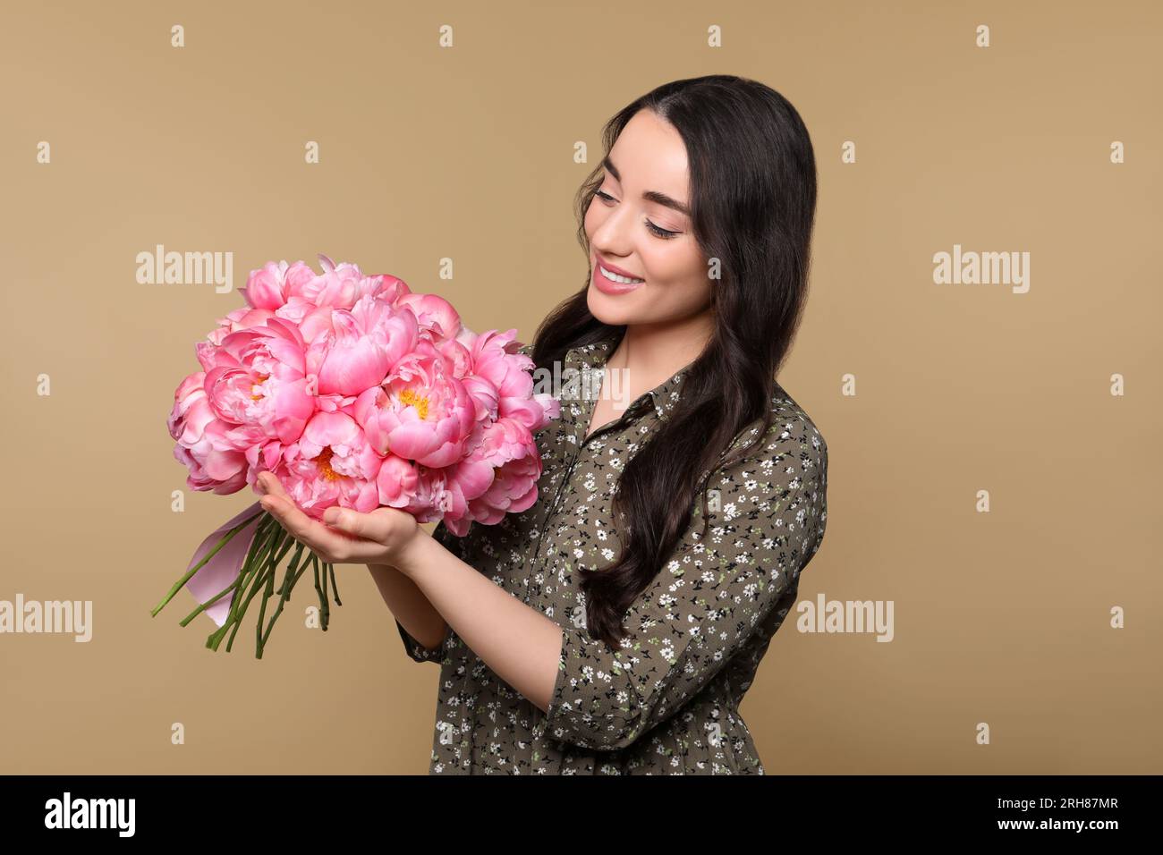 Beautiful young woman with bouquet of pink peonies on light brown ...