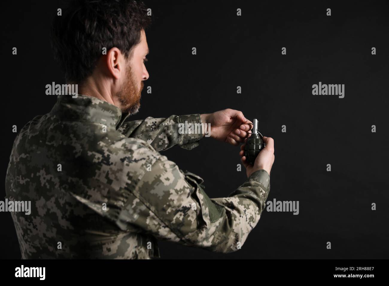 Soldier pulling safety pin out of hand grenade on black background