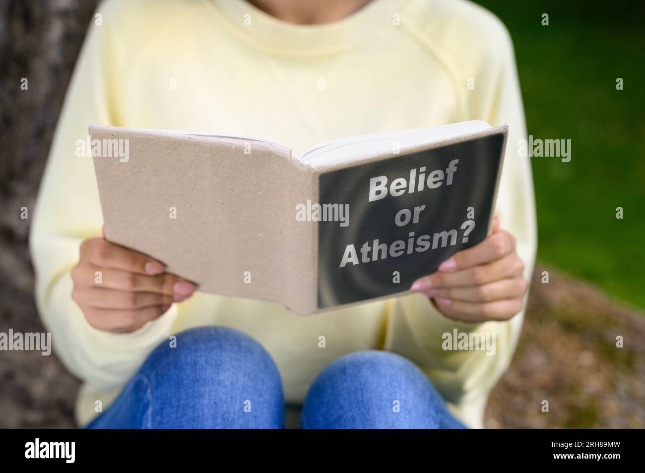 Woman reading book about belief and atheism outdoors, closeup Stock Photo