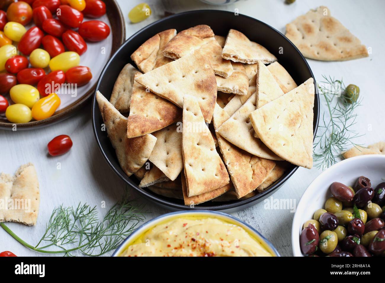 Mezze platter of pita bread surrounded by fresh tomatoes, olives and hummus over a white rustic table. Overhead view. Stock Photo