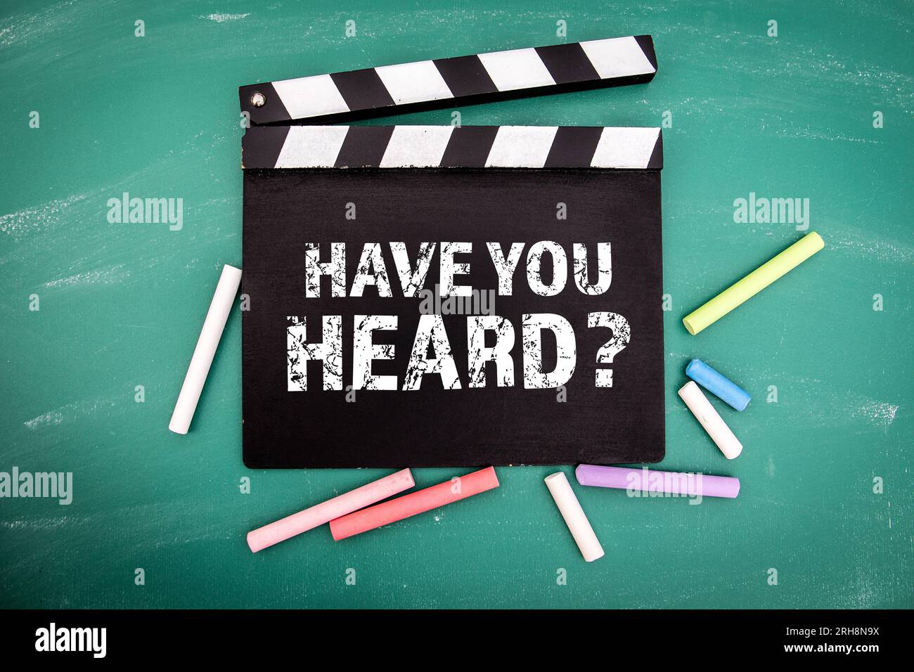 Have You Heard. Black movie clapper with chalk pieces on a green chalkboard background. Stock Photo