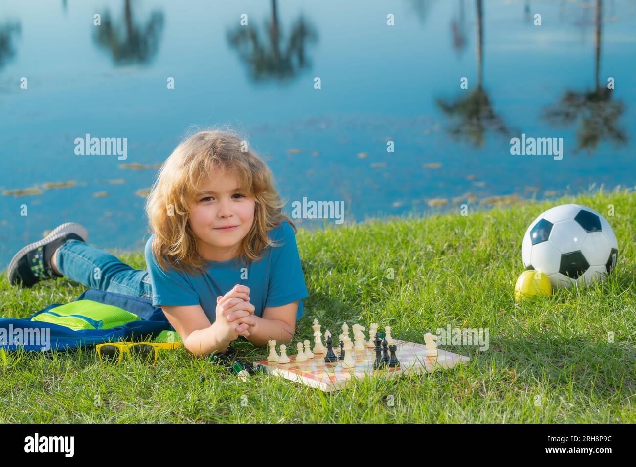 Kid thinking about chess laying on grass in summer park. The concept of learning and growing children. Chess, success and winning. Outdoor game, kids Stock Photo