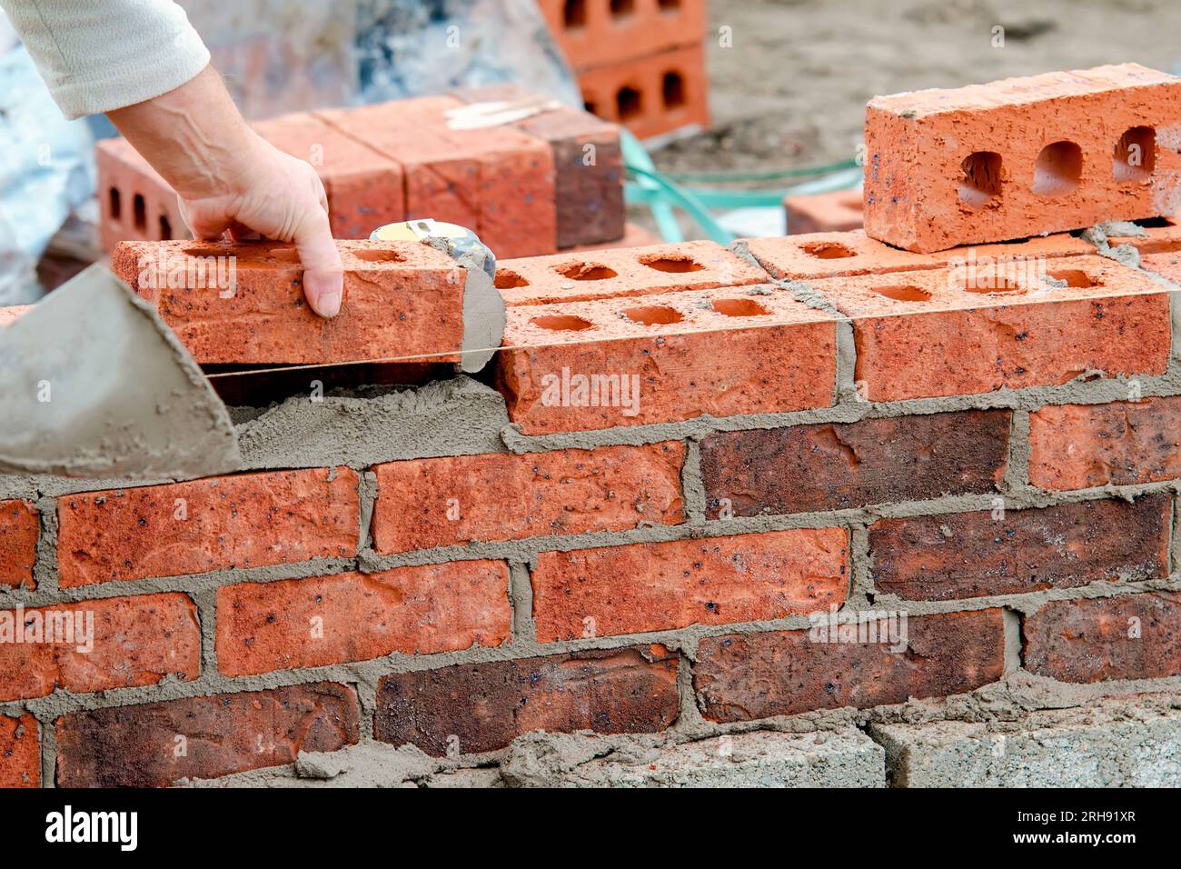 Hard working bricklayer lays bricks on cement mix on construction site