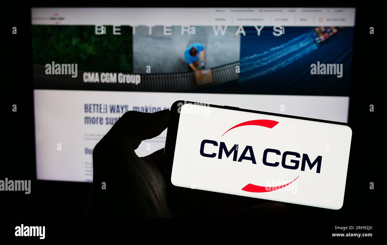 Person holding mobile phone with logo of French logistics company CMA CGM SA on screen in front of business web page. Focus on phone display. Stock Photo