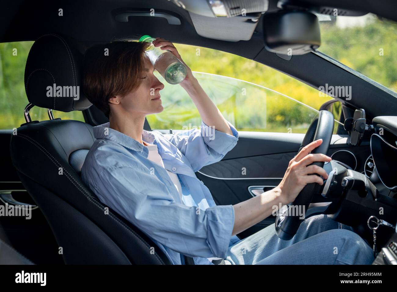 Suffering from heat exhausted woman driver sits in car put cold bottle to forehead with close eyes Stock Photo