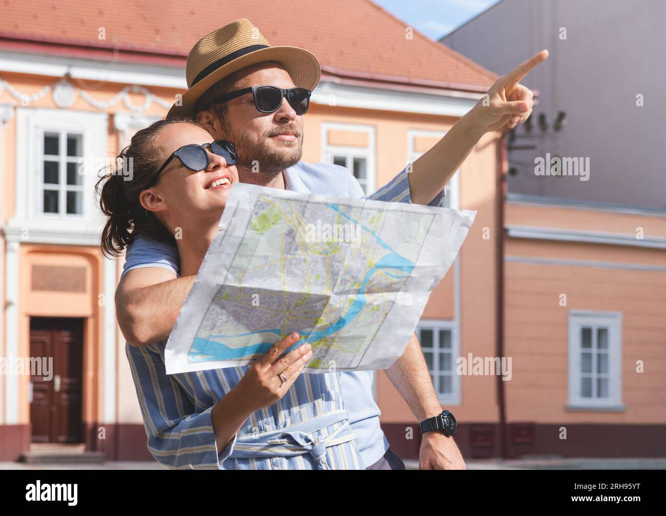 Young adult couple travellers with paper map in hands looking at historical attraction. Stock Photo