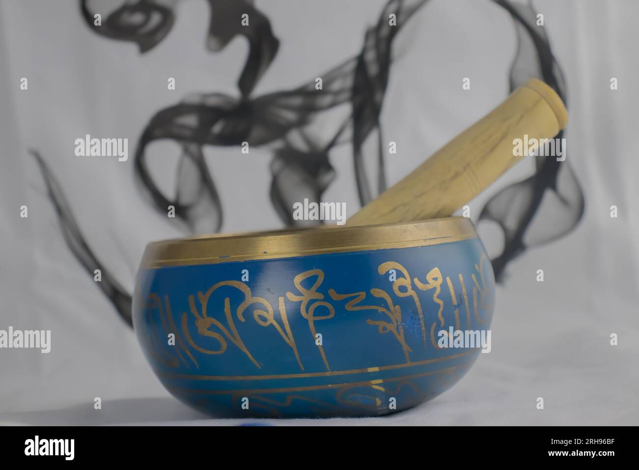 Hand Crafted bronze Singing Bowl painted in Blue and Gold color, often used for meditation, colorful background and OM symbol in background Stock Photo