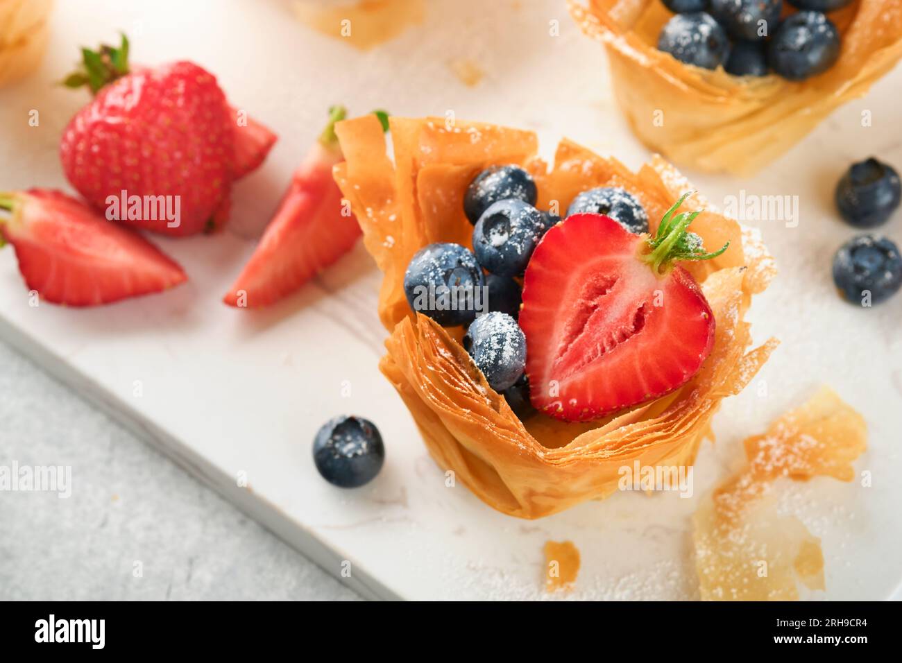 Phyllo or filo pies with fresh berries strawberries and blueberries, cheese filling topped with fresh mint on white plate. Homemade Filo pastry pasket Stock Photo
