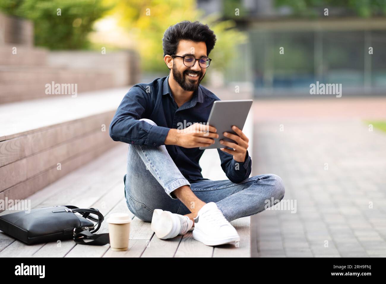 Positive indian guy resting at park after work, using tablet Stock Photo