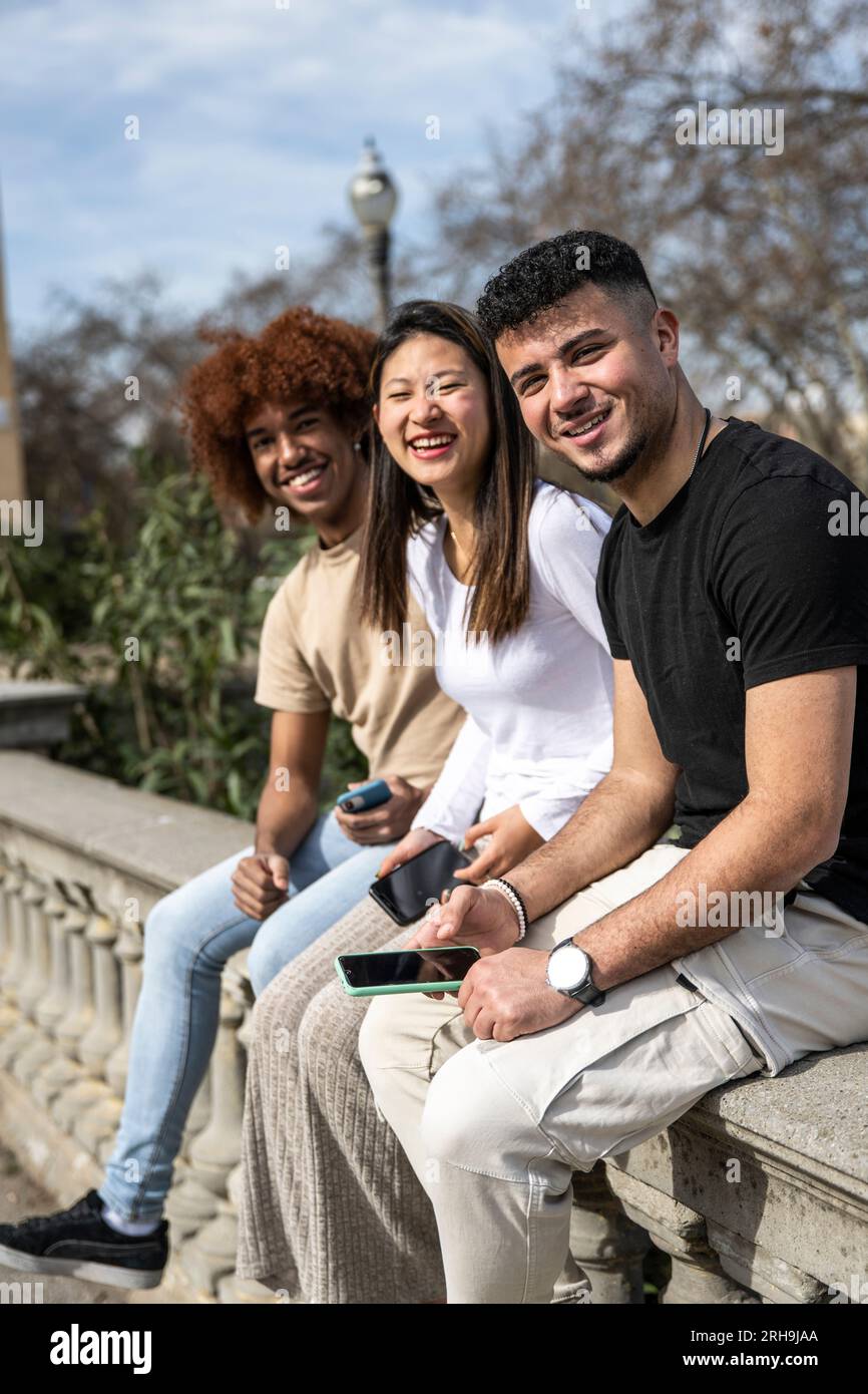 Three young diverse people with smartphones sitting on a balcony ...