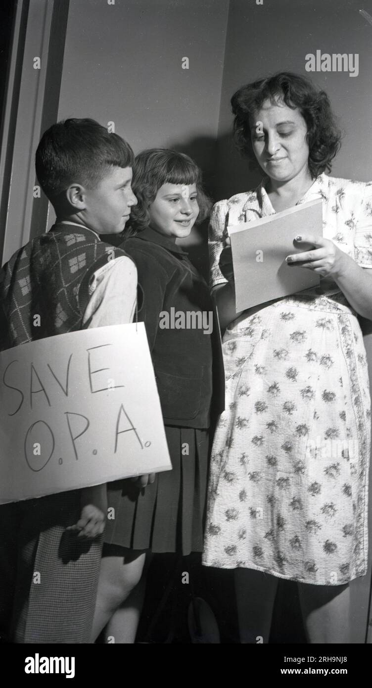 1946, historical, Challenger Club Kids...a boy and a girl stand outside the entrance of a property, watching as a woman puts her name down to supporting the O.P. A, New York, USA. They are holding handwritten placards saying Save OPA, which was the Office of Price Administration (OPA) which had been established in 1941 to control money (price controls to reduce inflation) and rents at the start of WW11. Stock Photo