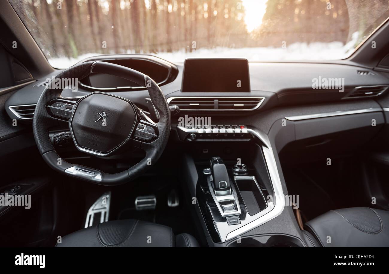 Interior of Peugeot 3008 parked in winter forest. Dashboard, center console, leather seats in the foreground and snow covered forest in the background Stock Photo