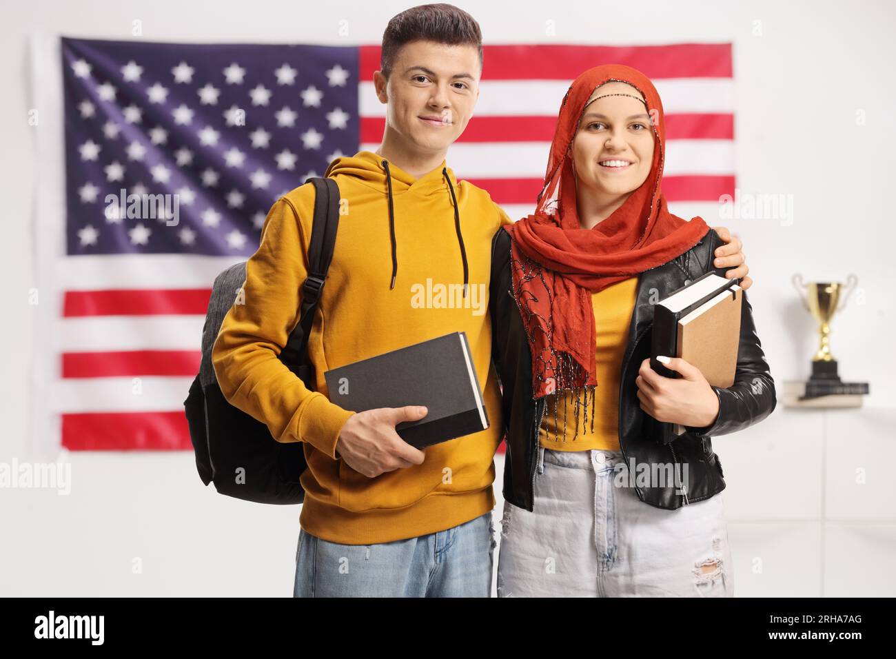 Young male and female student with a hijab holding books in front of an ...