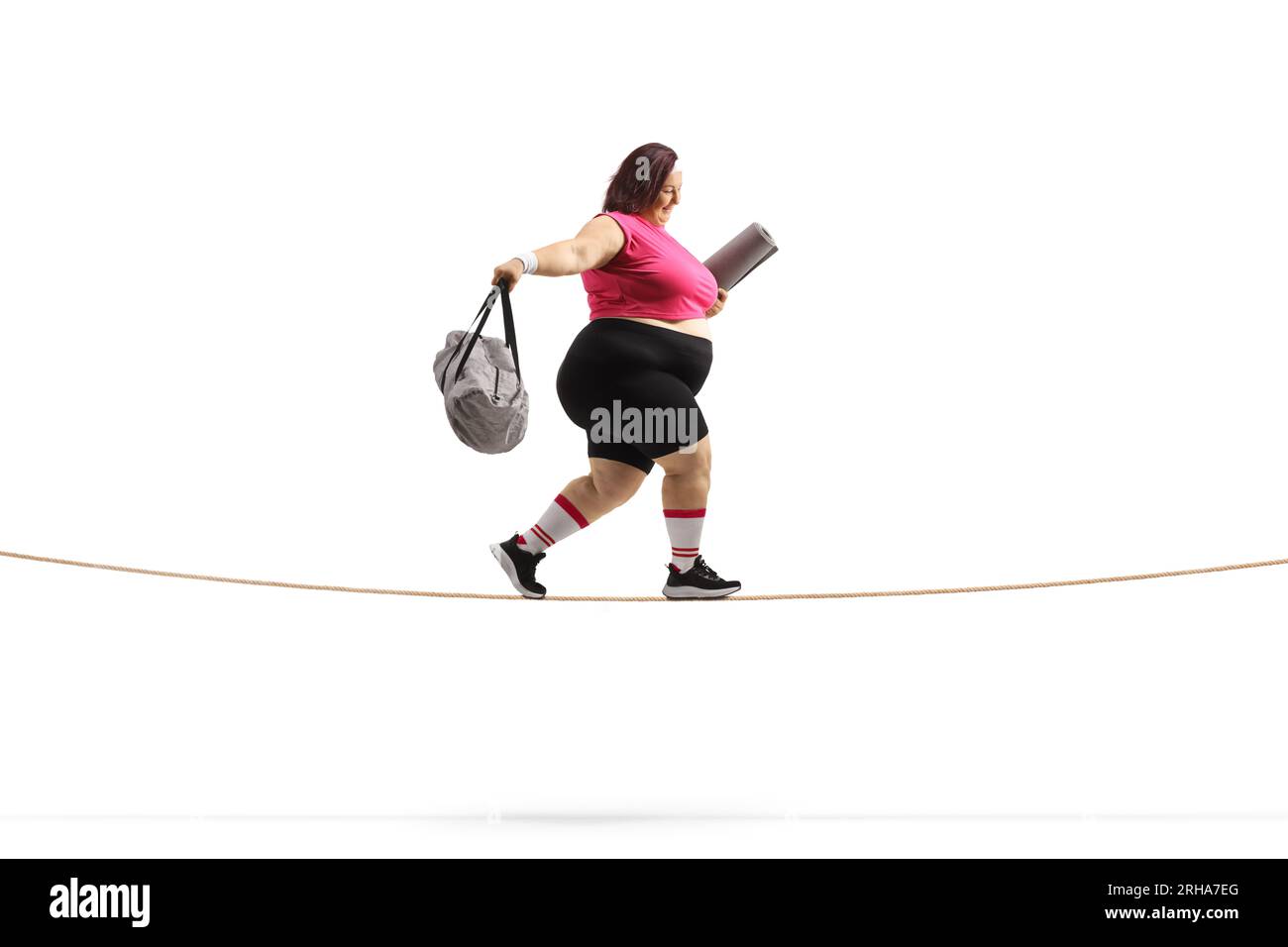 Side shot of an overweight woman with a sports bag and ezercise mat walking on a tightrope isolated on white background Stock Photo