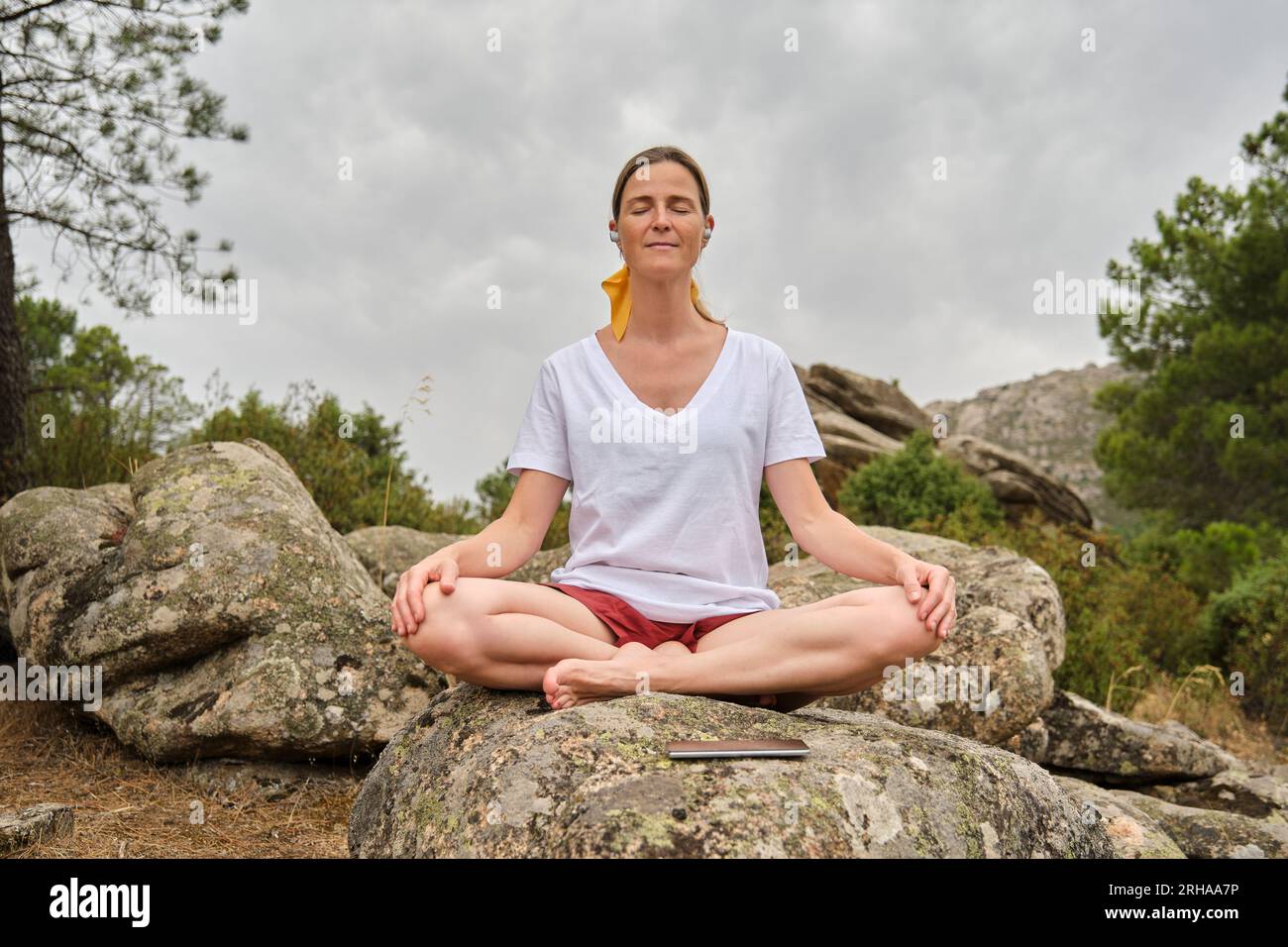 A Woman with smartphone sitting in lotus pose on rock Stock Photo