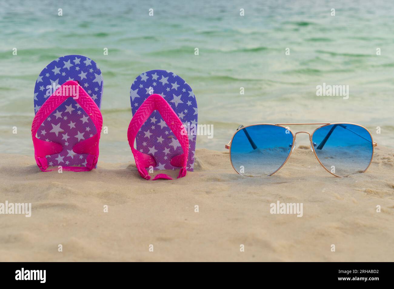 Blue sunglasses and flip flops lie in the sand on the beach near the ...