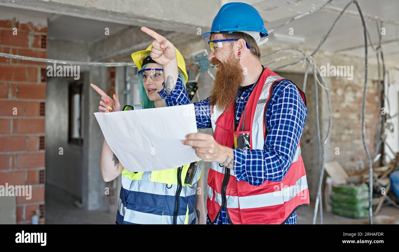 Man and woman builders reading house project speaking at construction site Stock Photo