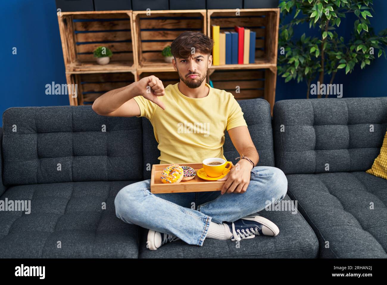 Arab man with beard sitting on the sofa at home eating breakfast with ...