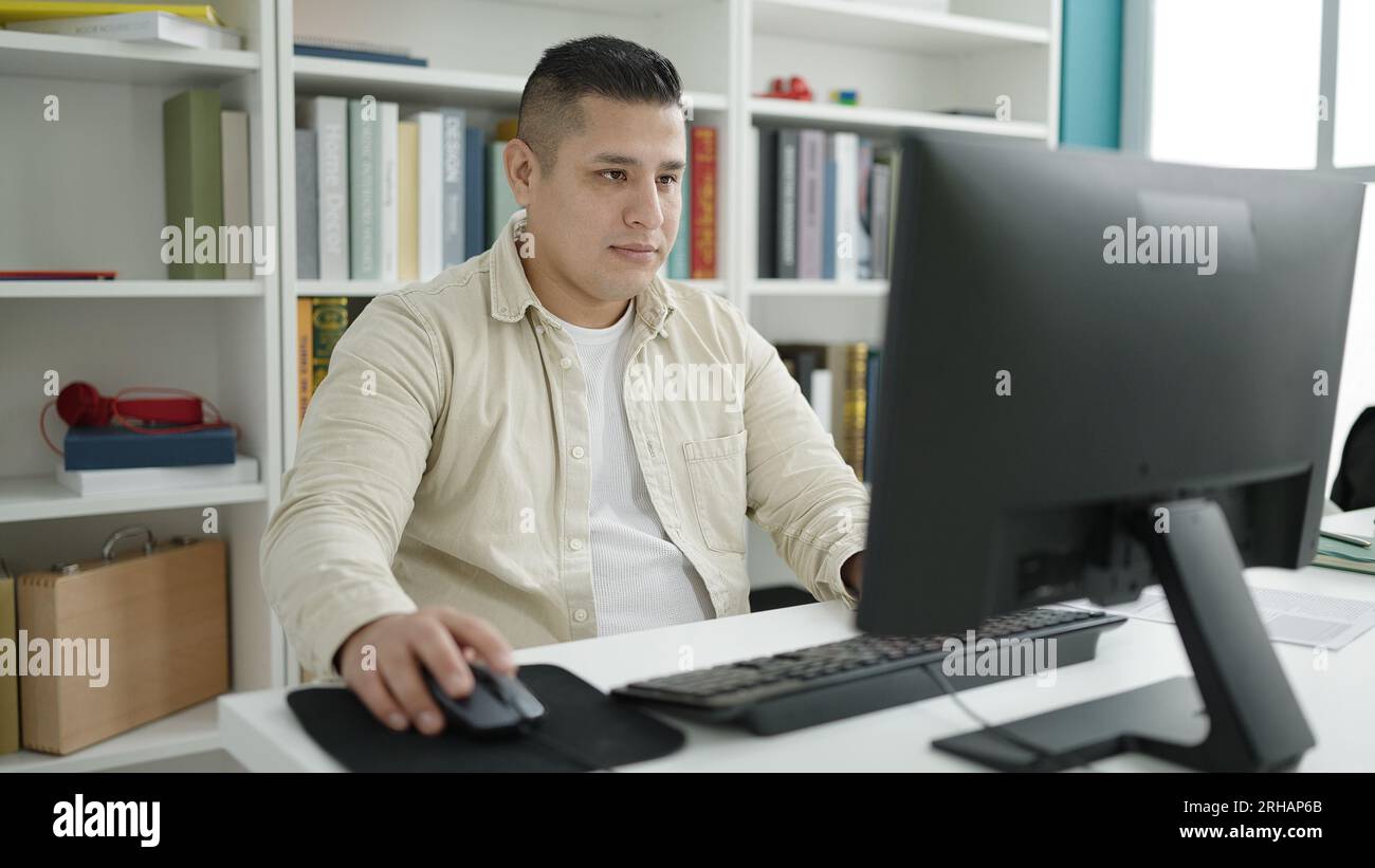 Young hispanic man student using computer studying at library ...
