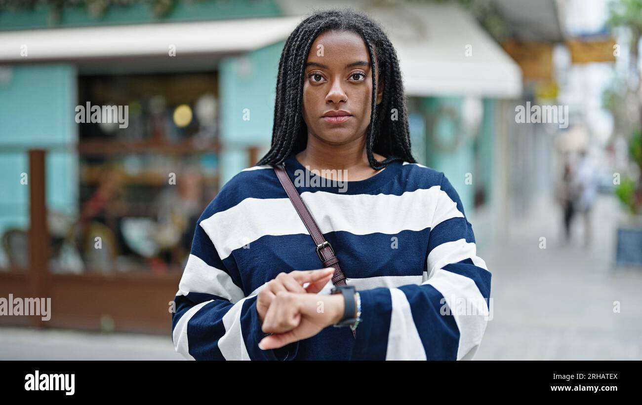 African american woman touching watch with finger waiting with serious ...