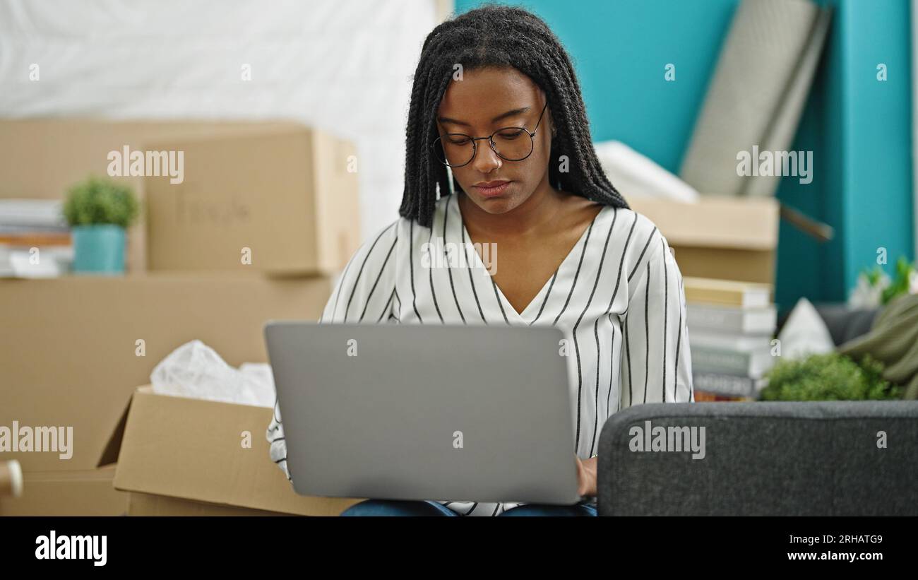 African american woman using laptop sitting on sofa at new home Stock ...