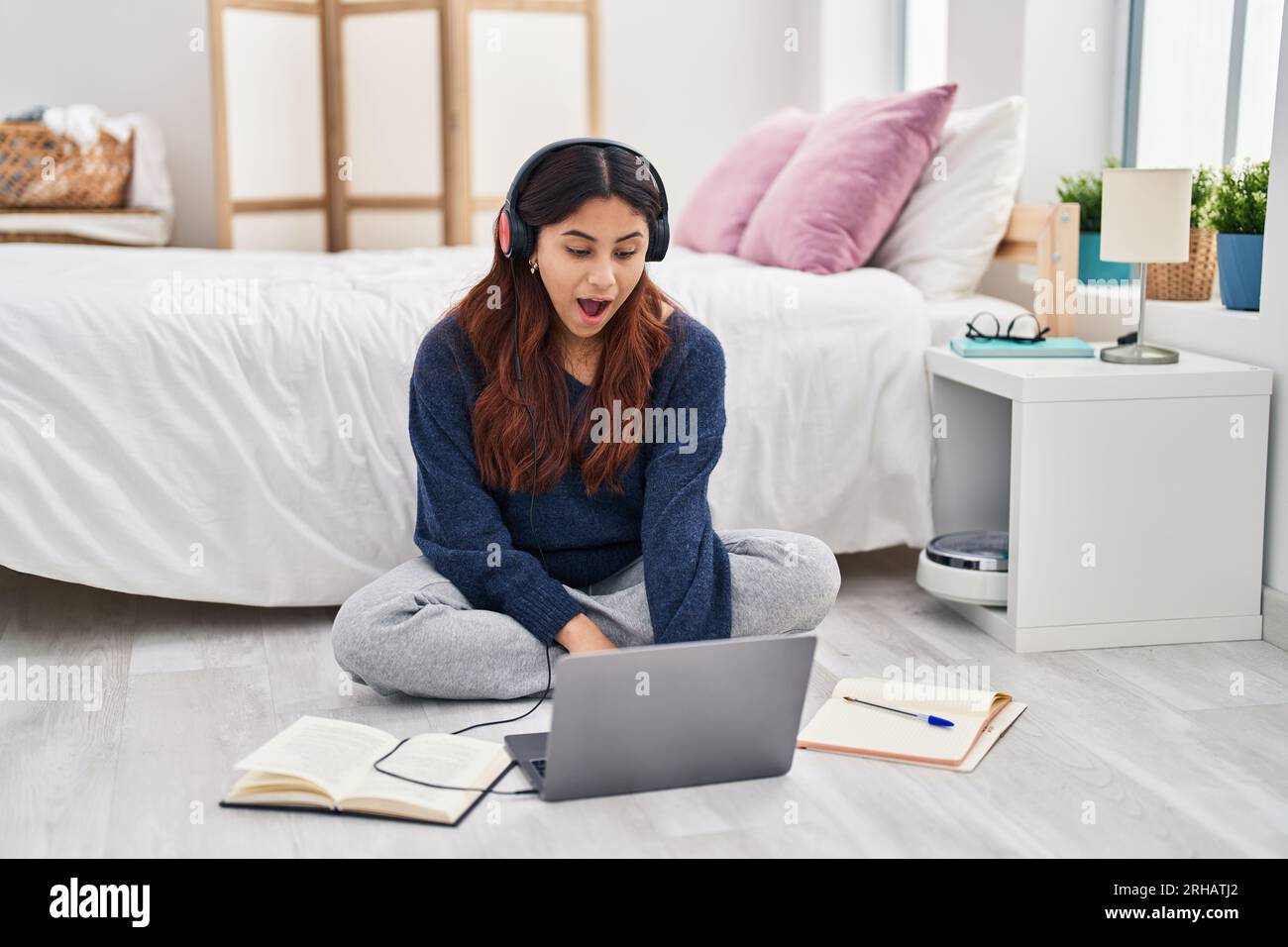 Hispanic young woman using laptop sitting on the floor at the bedroom ...