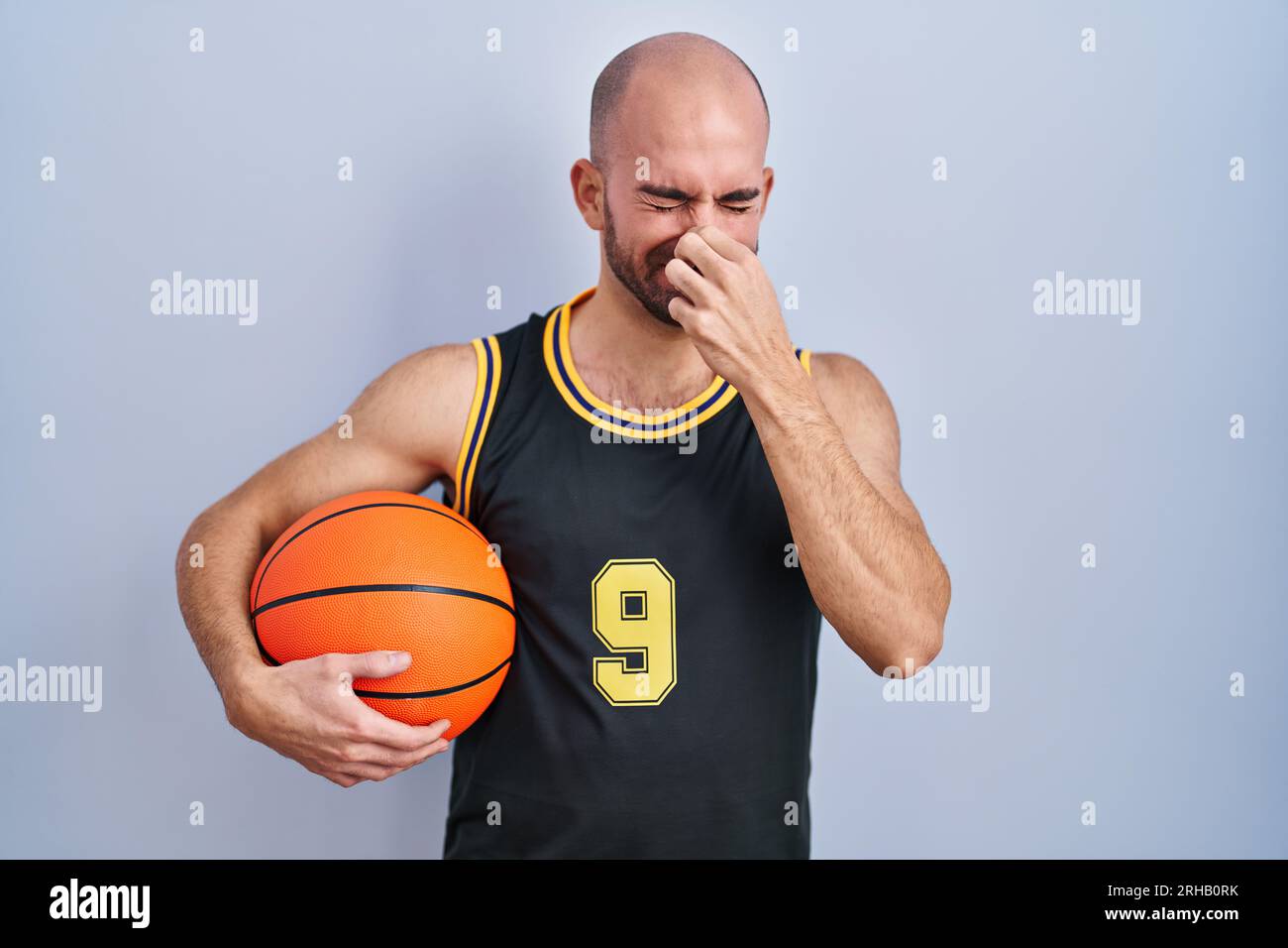 Young bald man with beard wearing basketball uniform holding ball