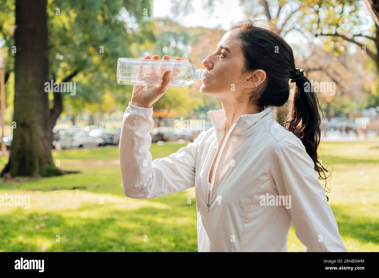 Middle age woman in profile drinking water after training in the park. Stock Photo