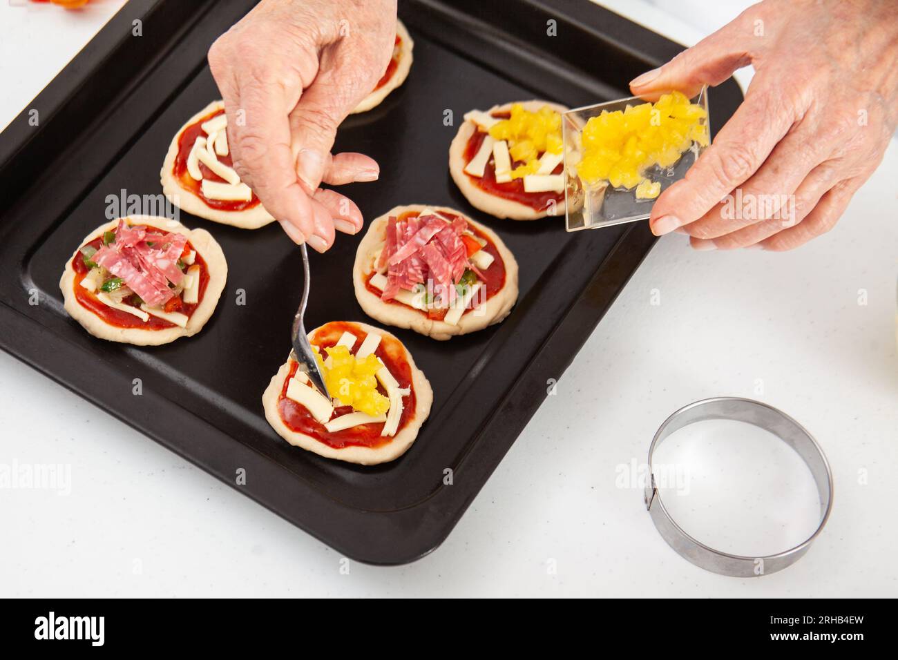 Adding toppings to the mini pizzas. Adding pineapple to the Hawaiian