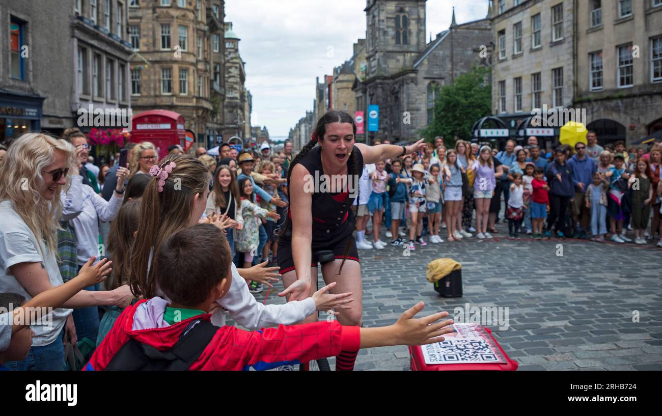 Royal Mile, Edinburgh, Scotland, UK. 15 August 2023. People still migrating to the High Street for street entertainment and to discover what shows are still available, street performers getting reasonable audiences to watch them demonstrate their skills. Temperature around 19 degrees centigrade with sunshine in morning and cloud in the afternoon. Pictured: Street performer Luth gets high fives all round from her audience. Credit: Archwhite/alamy live news. Stock Photo