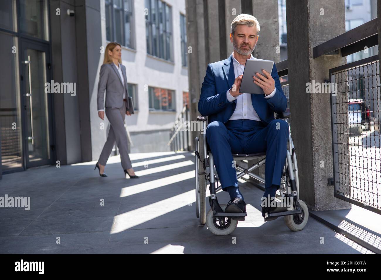 Executive business man in wheelchair with tablet using mobile device for work outdoors. Stock Photo