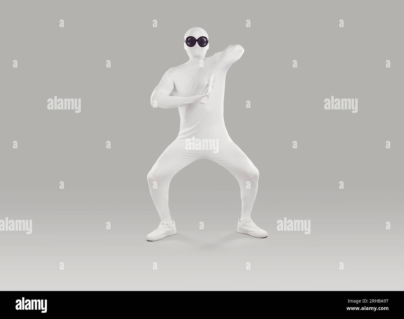 Funny man wearing white spandex bodysuit and glasses dancing on gray studio background Stock Photo