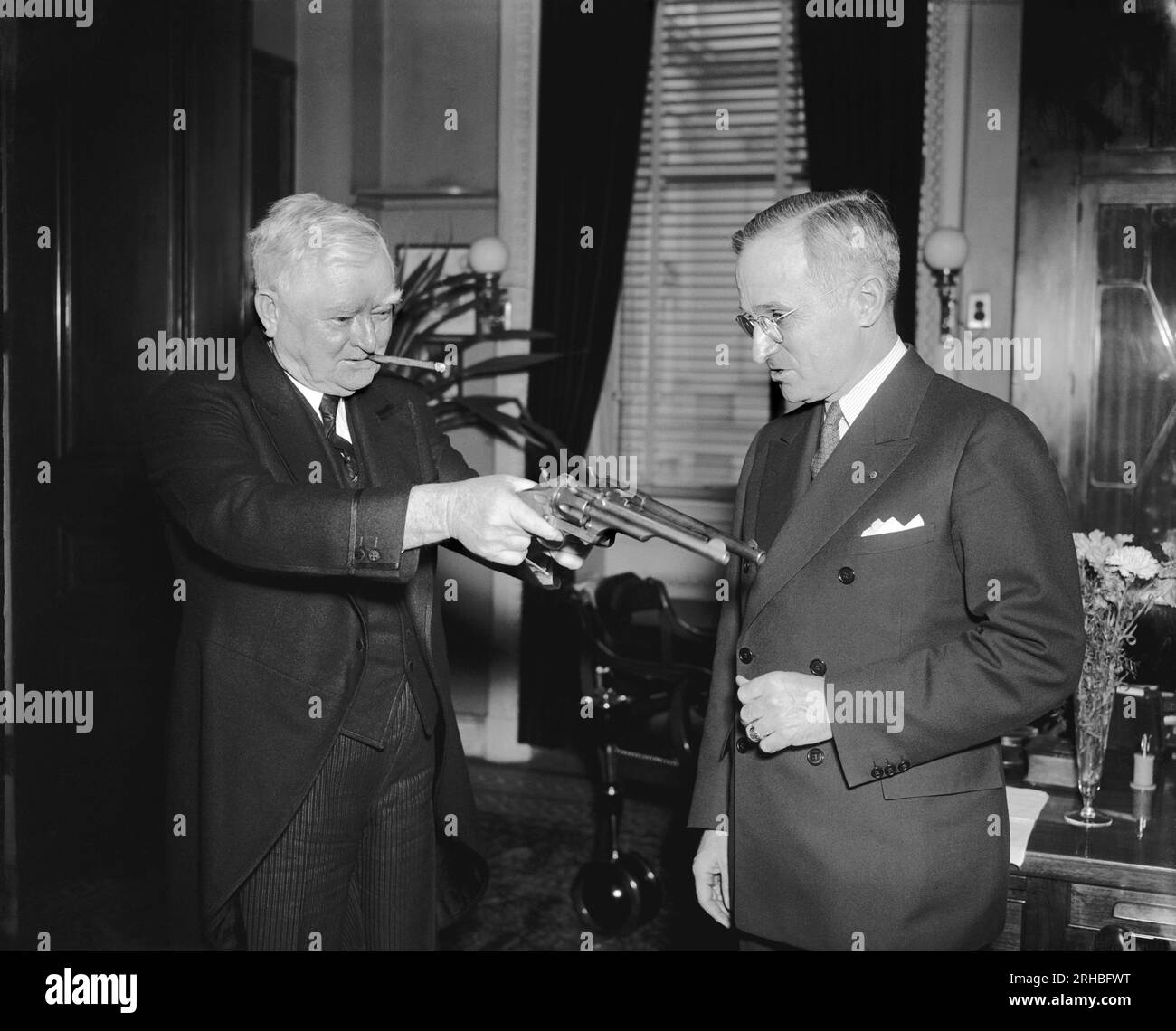 Washington, D.C.:   February 17, 1938  Vice President Garner playfully tries his 'stickup' technique on Senator Harry Truman of Missouri, present owner of the .45 pistols that were formerly used by Jesse James. Senator Truman secured the guns in Southern Missouri from a doctor's wife, whose husband received them in payment of medical services rendered to Frank James, another of the James' boys. Jesse James had previously left them to Frank after he was killed by the Pinkerton men. The bandit garnered nearly $1,000,000 in a series of holdups with the guns. Stock Photo