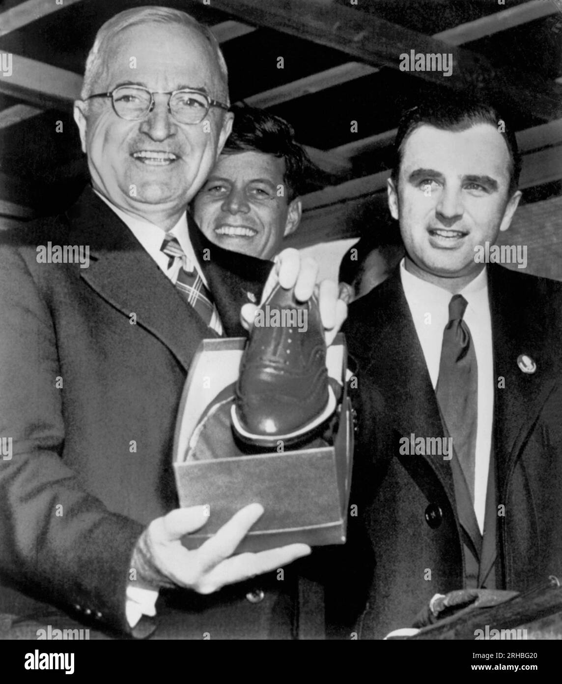 Brockton, Massachusetts:  October 18, 1952 President Truman displays a pair of shoes presented to him by Mayor Lucey (r) in this shoe center as the President continued his whistle stop tour of New England in his campaign for Democratic candidate Adlai Stevenson.  John F. Kennedy, who was not noted in the press release, stands in the background. Stock Photo